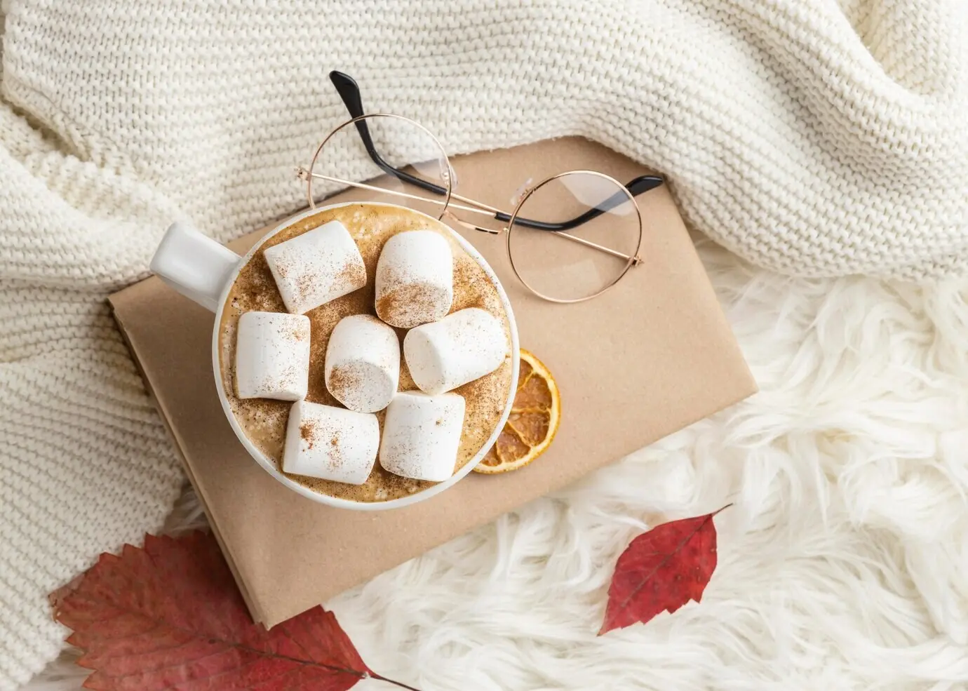 Вид сверху на чашку горячего какао с маршмеллоу на книге с очками.